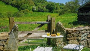 A rustic outdoor seating area with a stone table, two chairs, and a wooden gate. - Escape to an Idyllic Countryside Couple's Retreat (Totnes)