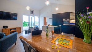 A modern living room with a wooden dining table, a sofa, and a television. - Relaxed Devon Stay Close to fabulous Beaches (Slapton)