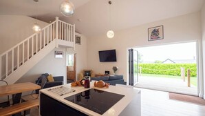 A modern kitchen with a central island, a dining area with a bench, a staircase, and a large sliding glass door leading to a garden. - Relaxed Devon Stay Close to fabulous Beaches (Slapton)