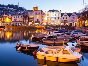 A harbor with boats docked, buildings with lights, and a calm water reflecting the scene.