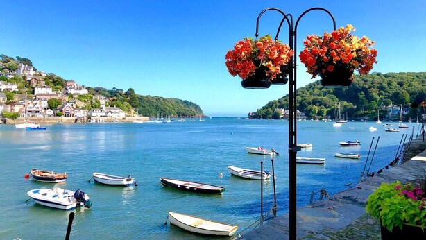 Una cittadina costiera con barche ormeggiate lungo il lungomare, un cielo azzurro e limpido e edifici su una collina.