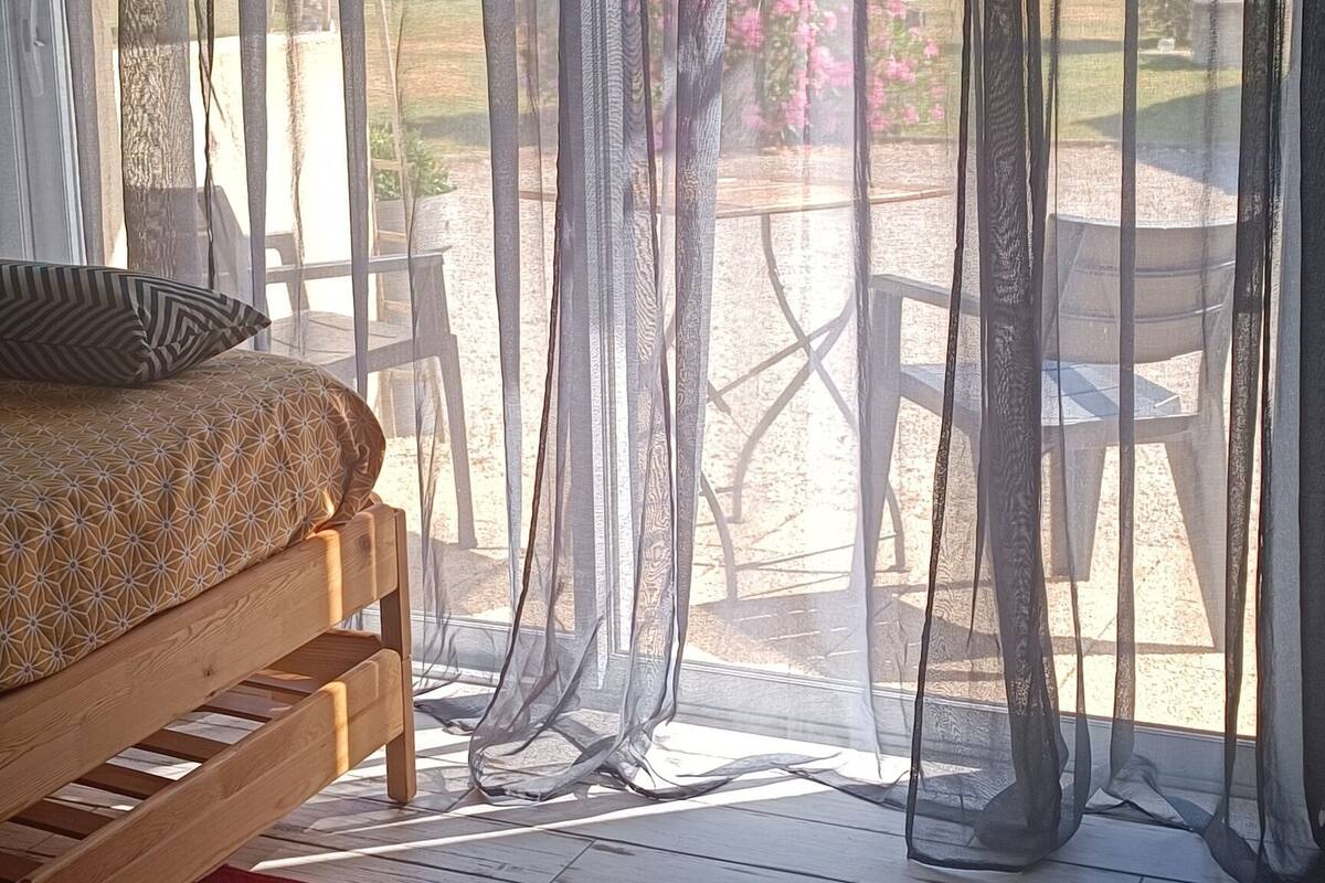 A bedroom with a bed, a red rug, and sheer curtains.