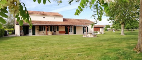 A two-story house with a covered patio, a lawn, and a tree.