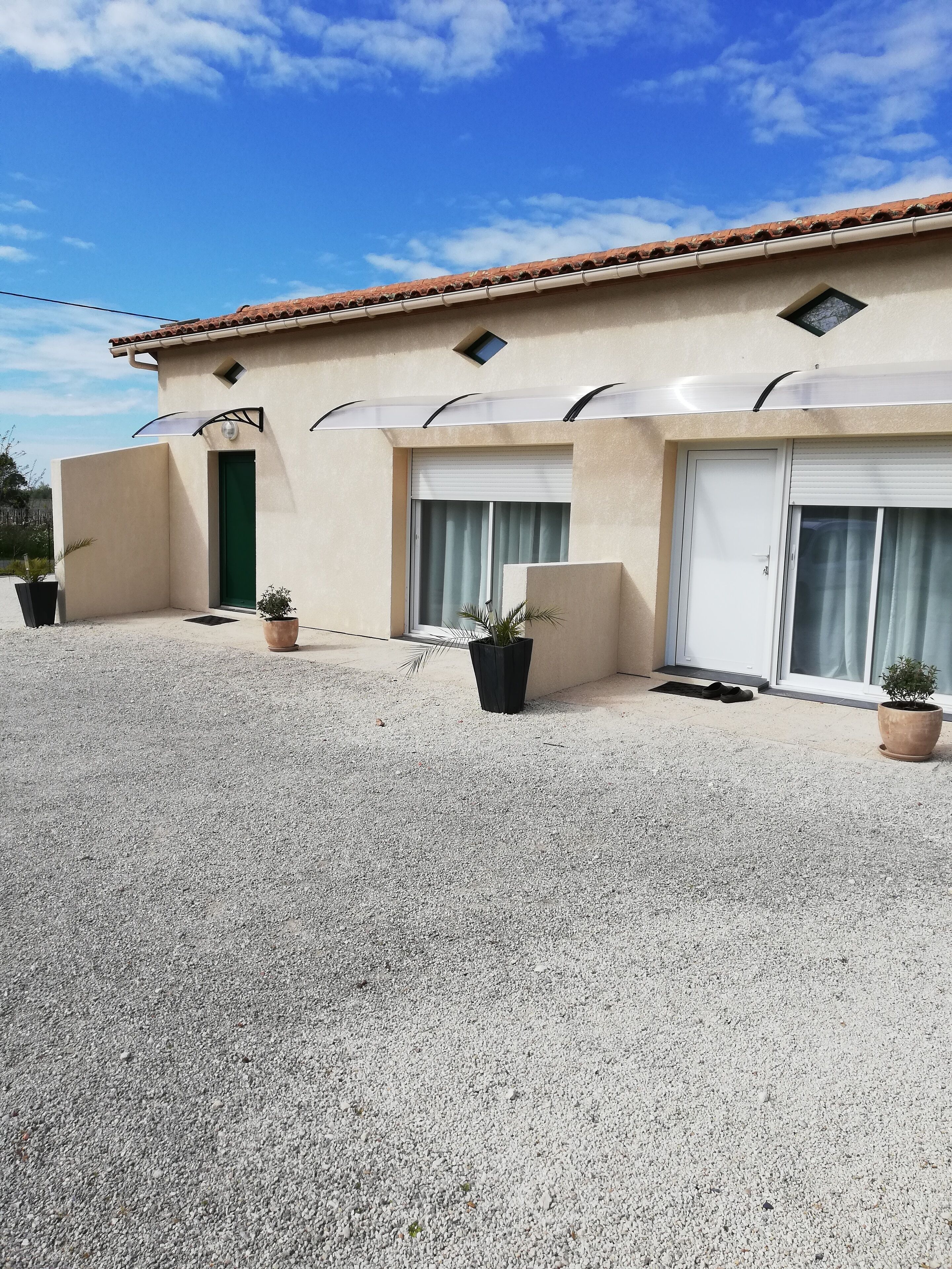 A building with a tiled roof, a green door, and a gravel driveway.
