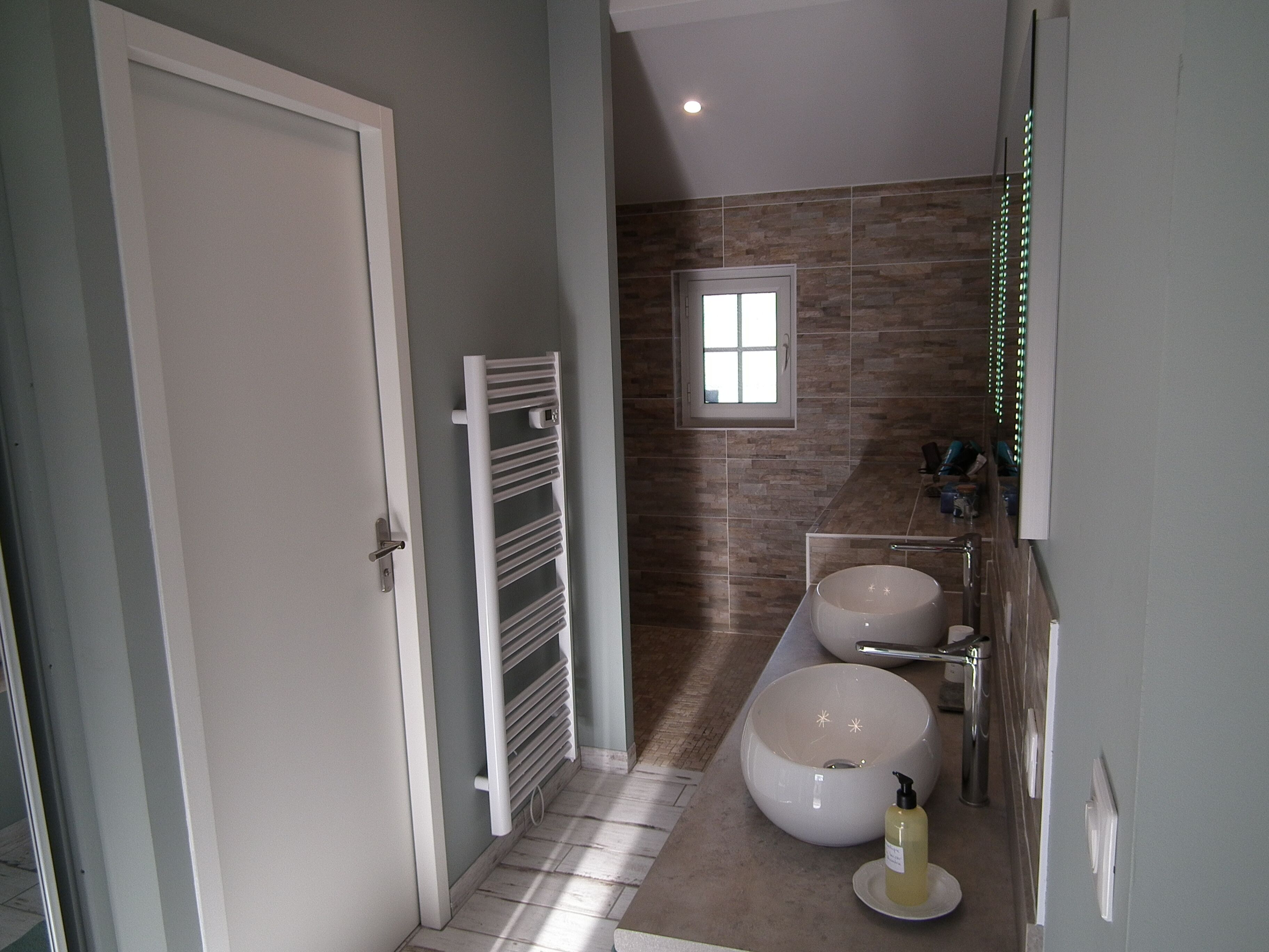 A modern bathroom with a walk-in shower, two sinks, a towel rack, and a window.