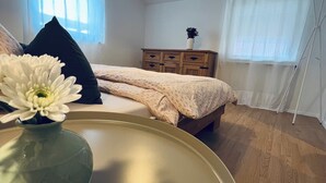 A bedroom with a bed, a dresser, a vase with a flower, and a hanging light fixture.