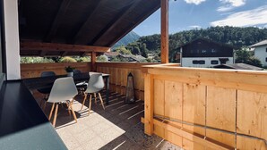 A wooden deck with a table and chairs, overlooking a mountainous landscape.
