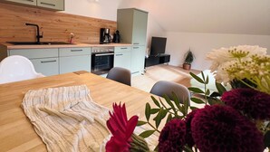 A modern kitchen with wooden beams, a dining area with a table set for two, and a view of the living room.