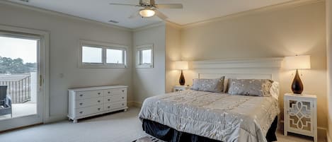 Ein Schlafzimmer mit einem Bett, zwei Nachttischen, einem Deckenventilator, einem Schminktisch und Blick durch eine Schiebetür.