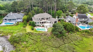 A large, two-story house with a swimming pool, surrounded by lush greenery and tall trees. - 28 Oyster Landing -  A Magnificent Marsh View in Sea Pines! (Hilton Head Island)
