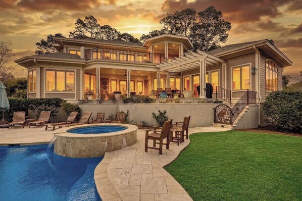 Una casa grande con piscina, zona de estar exterior y una escalera que lleva a la planta superior.