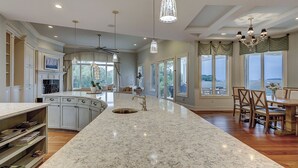 A spacious kitchen with a central island, large windows, and a dining area with a view. - 28 Oyster Landing -  A Magnificent Marsh View in Sea Pines! (Hilton Head Island)