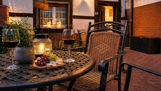 An outdoor dining area with a round metal table, wicker chairs, a potted plant, a lantern, and a sign above the door. - Quiet vacation apartment with two bedrooms Bad Muskau - Fürst Pückler Park (Bad Muskau)