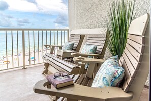 A balcony with two wooden lounge chairs, one with a book and glasses, and a view of the beach.