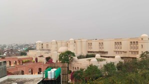 Un grand bâtiment historique doté de plusieurs dômes et de fenêtres en arc, entouré de verdure et d’autres bâtiments.
