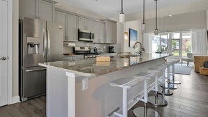 A modern kitchen with stainless steel appliances, a granite countertop, and bar stools. - Amenity filled Peninsula!  24242 Canoe (Millsboro)