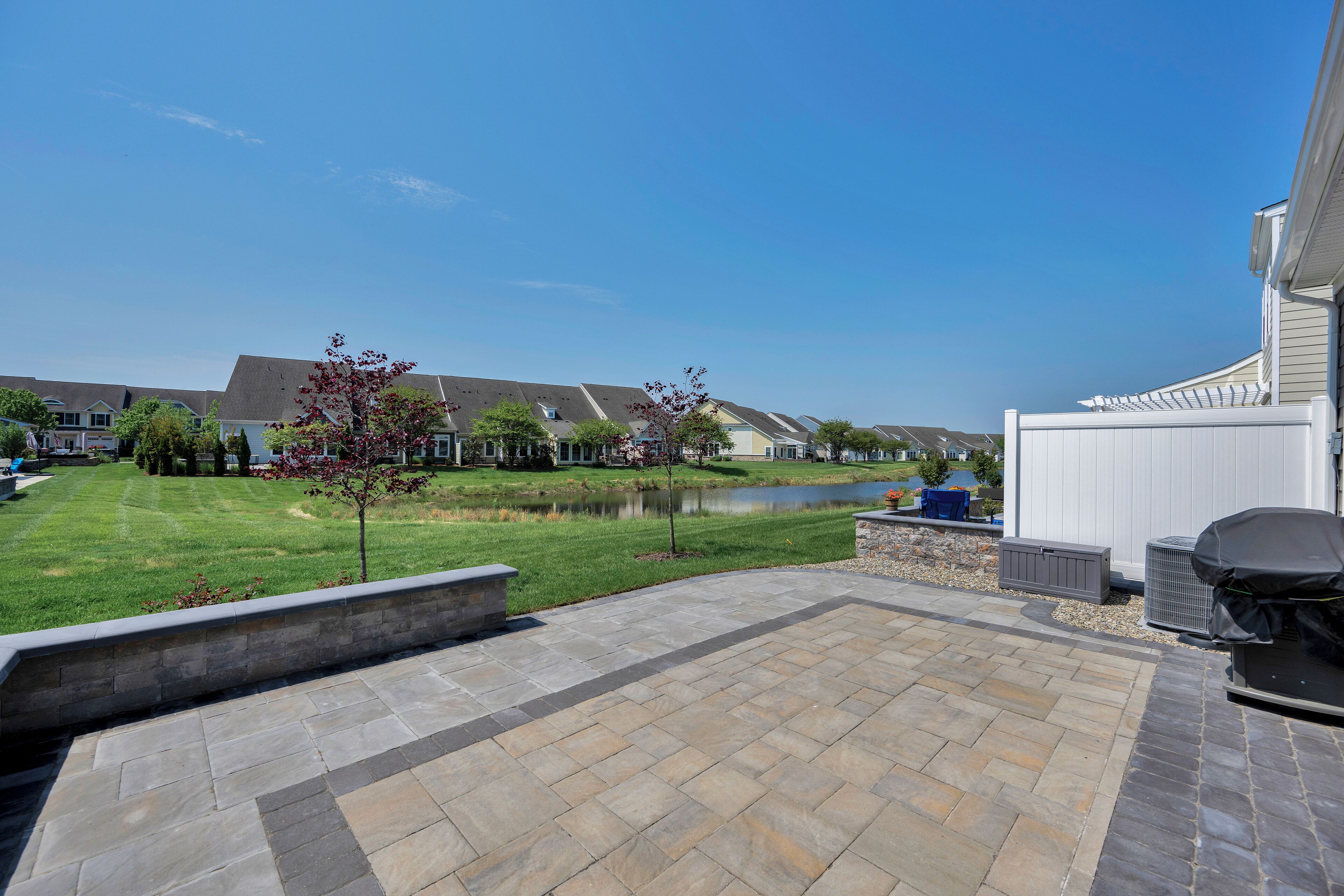 Un espace patio avec des carreaux de pierre, un barbecue et une vue sur un lac et des maisons au loin.
