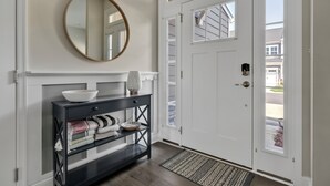 A hallway with a white door, a black console table with a bowl and folded towels, and a round mirror on the wall. - Amenity filled Peninsula!  24242 Canoe (Millsboro)