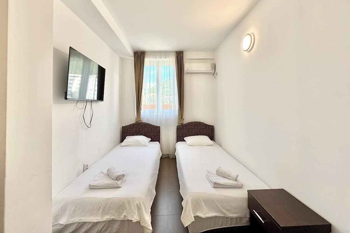 Una habitación de hotel con dos camas, televisión, aire acondicionado y una mesita de noche.
