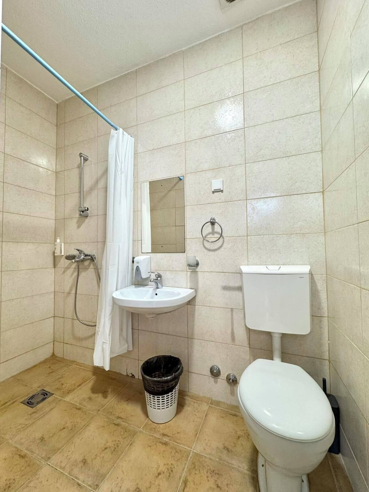 A small bathroom with a shower, sink, toilet, and a trash bin.