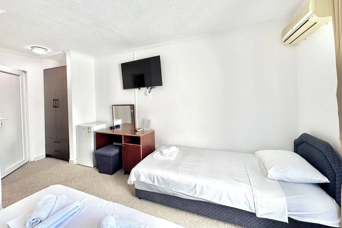 Una habitación de hotel con cama, escritorio, silla, televisor y aire acondicionado.