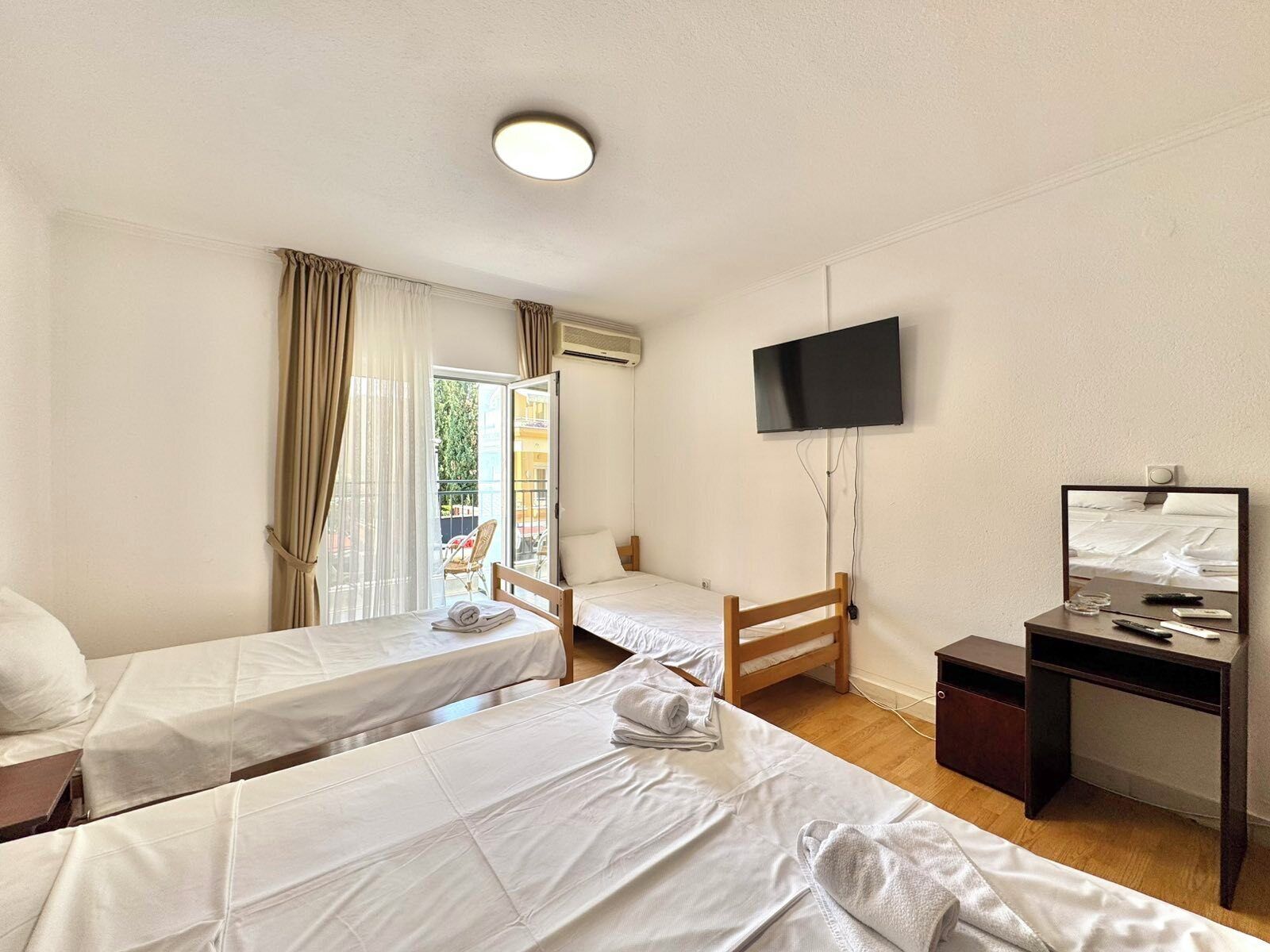 A hotel room with two single beds, a desk with a TV, and a sliding door to the balcony.