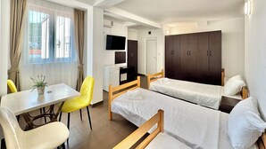 A hotel room with two single beds, a small table with a chair, a TV, and a wardrobe. - Hotel Lobo (Budva)