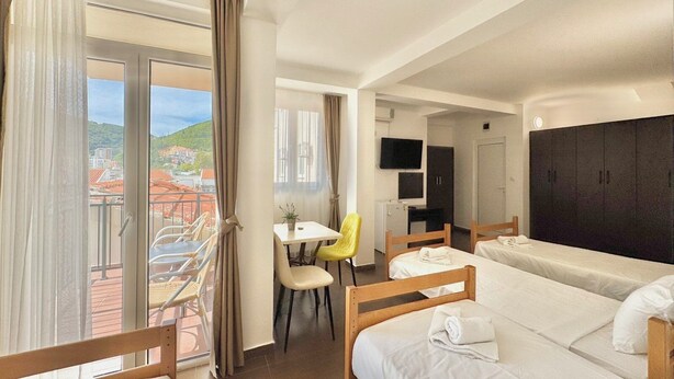 A hotel room with two beds, a dining area, a TV, and a view of the city. - Hotel Lobo (Budva)