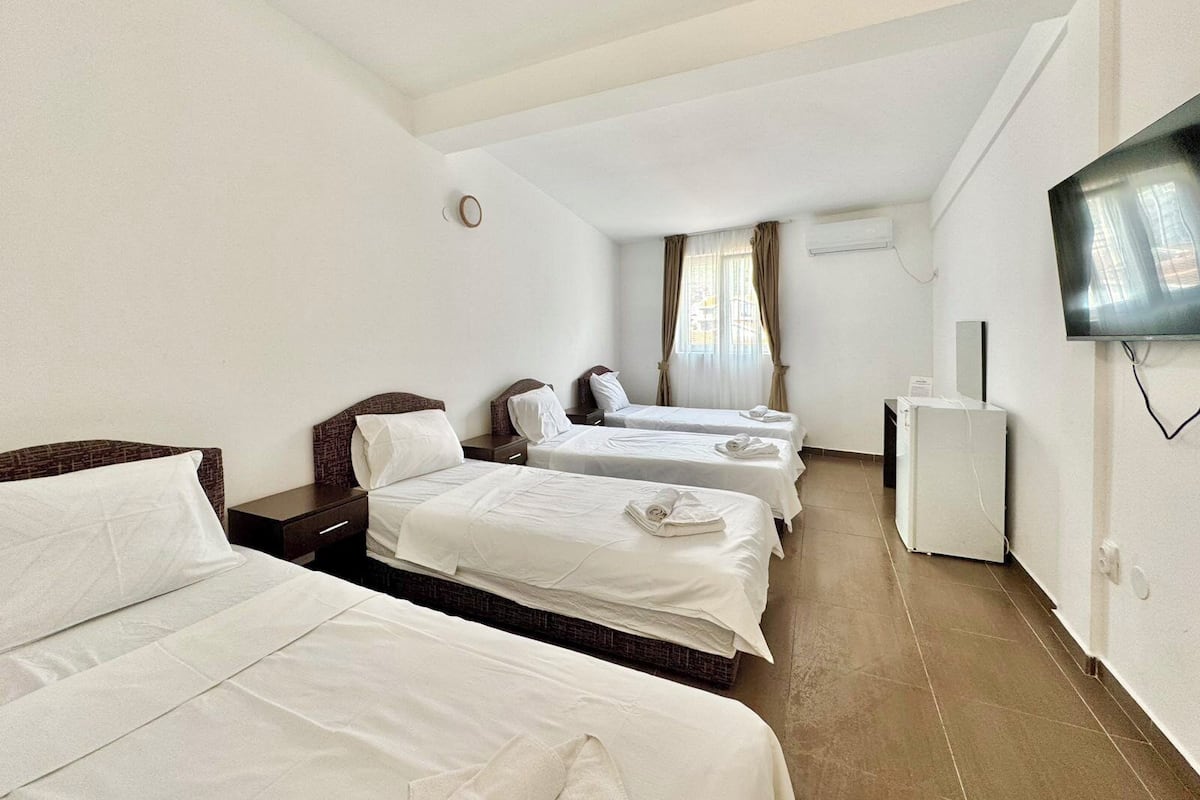 Habitación de hotel con tres camas, un televisor y un escritorio pequeño.