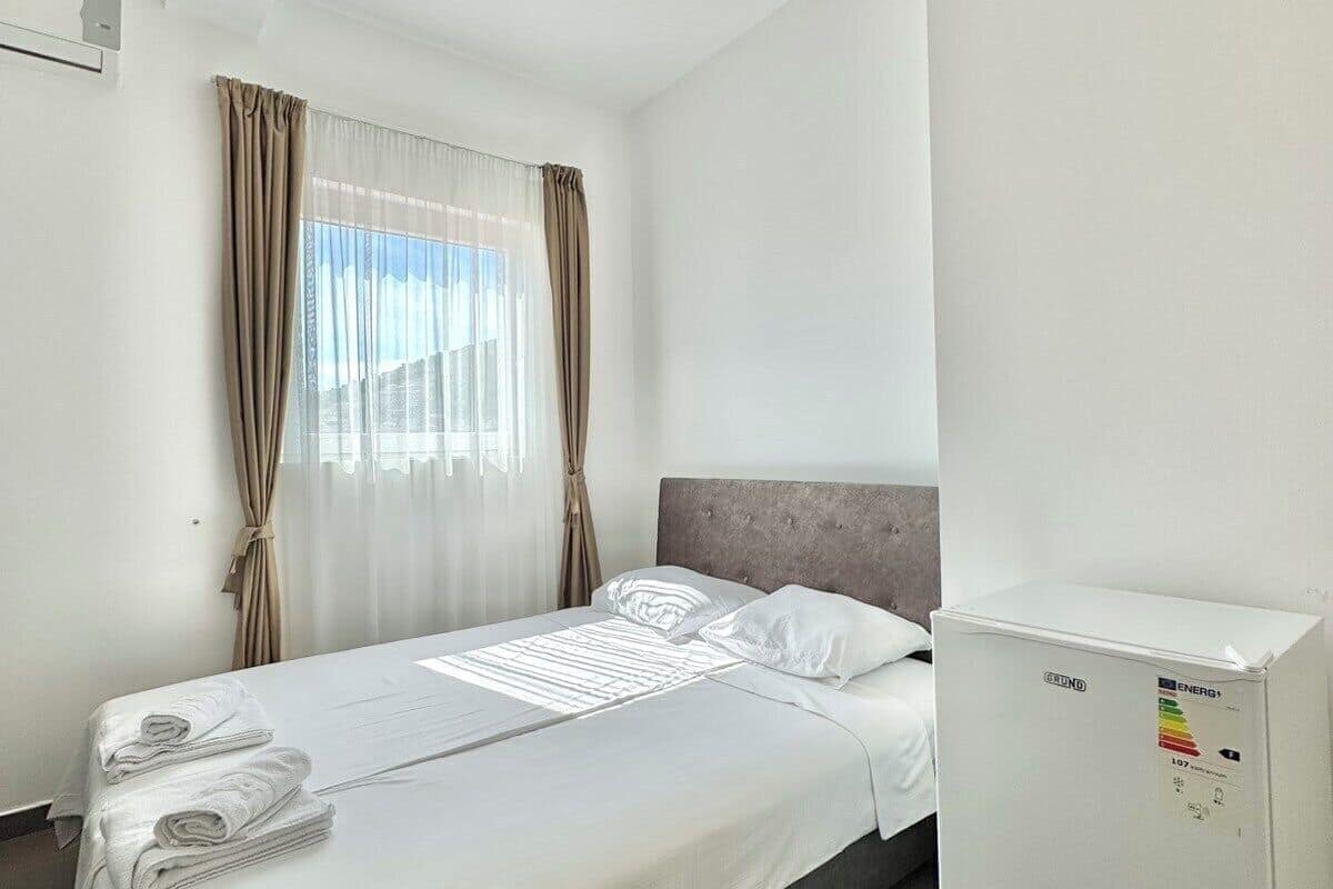 Habitación de hotel con cama, refrigerador y ventana con cortinas.
