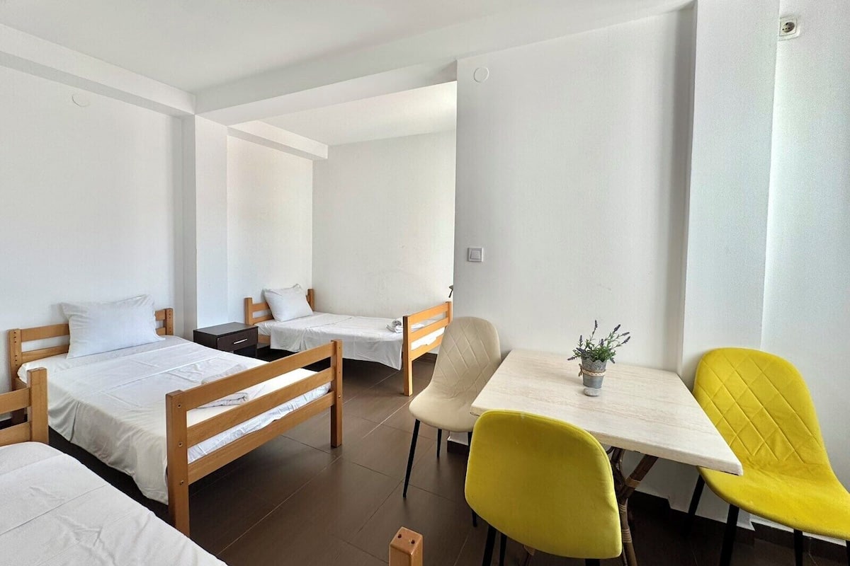Una habitación de hotel con dos camas individuales, una mesita con una planta en maceta y dos sillas amarillas.