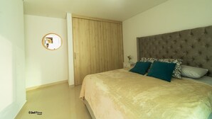 A bedroom with a bed, a wooden wardrobe, a round mirror, and a nightstand with a vase. - Modern apartment near the sea (Cartagena de Indias)