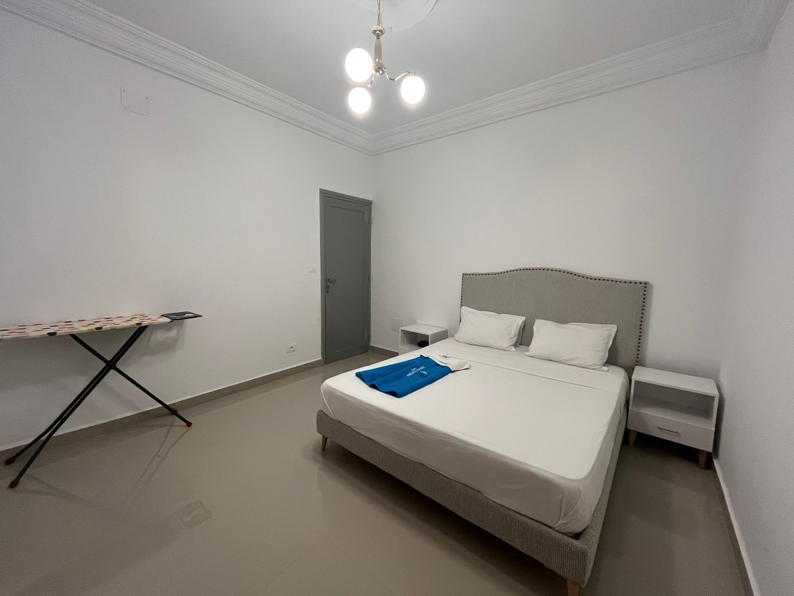Un dormitorio ordenado con cama, mesitas de noche, un escritorio y una puerta.