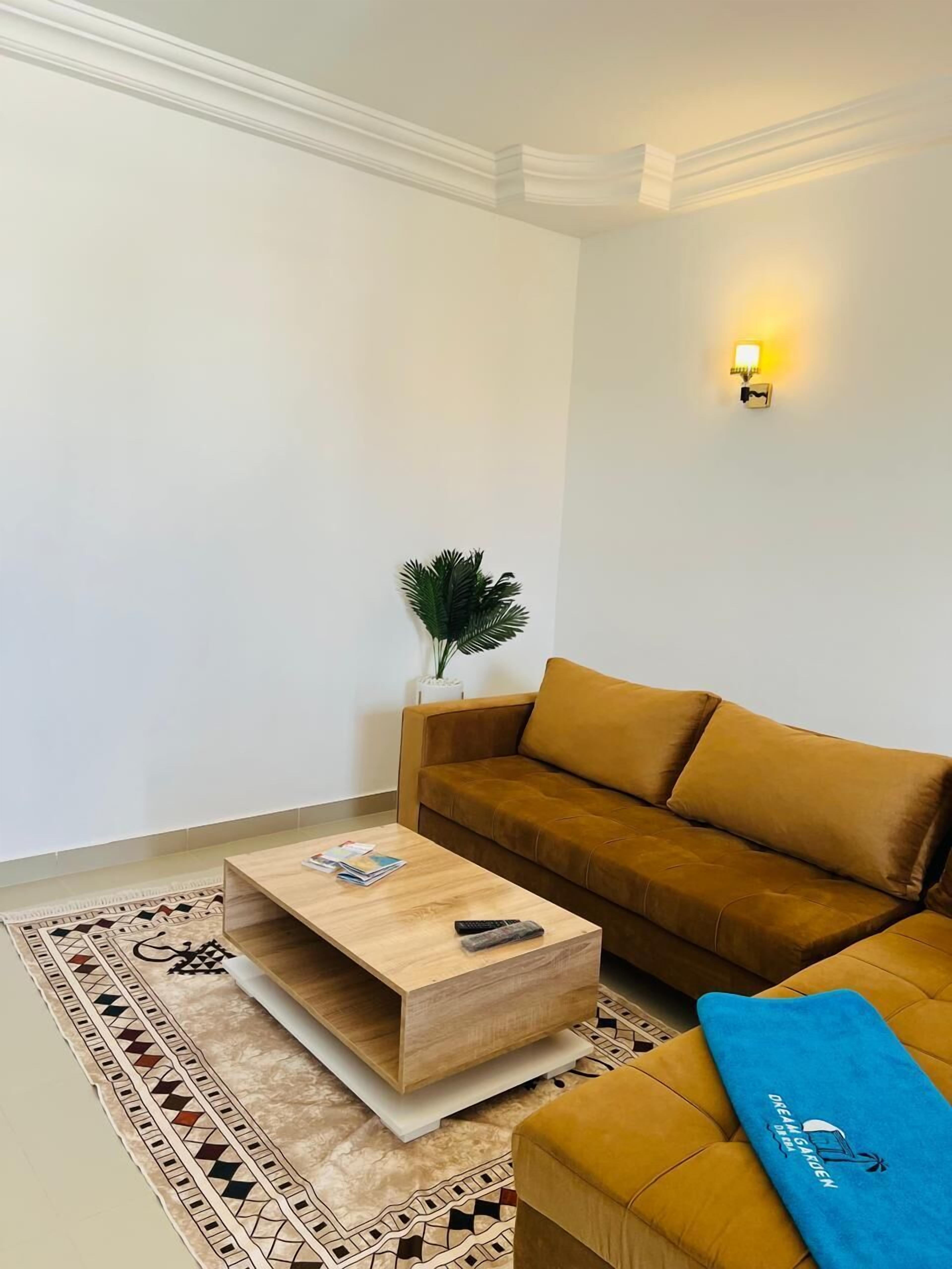 Un salon avec un canapé marron, une table basse en bois, un tapis à motifs et un luminaire fixé au mur.