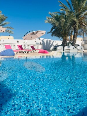 A clear blue pool with lounge chairs and umbrellas, surrounded by palm trees and a white building. - Dream Garden Djerba (Mezraia)