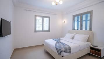 Ein Schlafzimmer mit einem Bett, einem Fernseher, einem Nachttisch und zwei Fenstern.