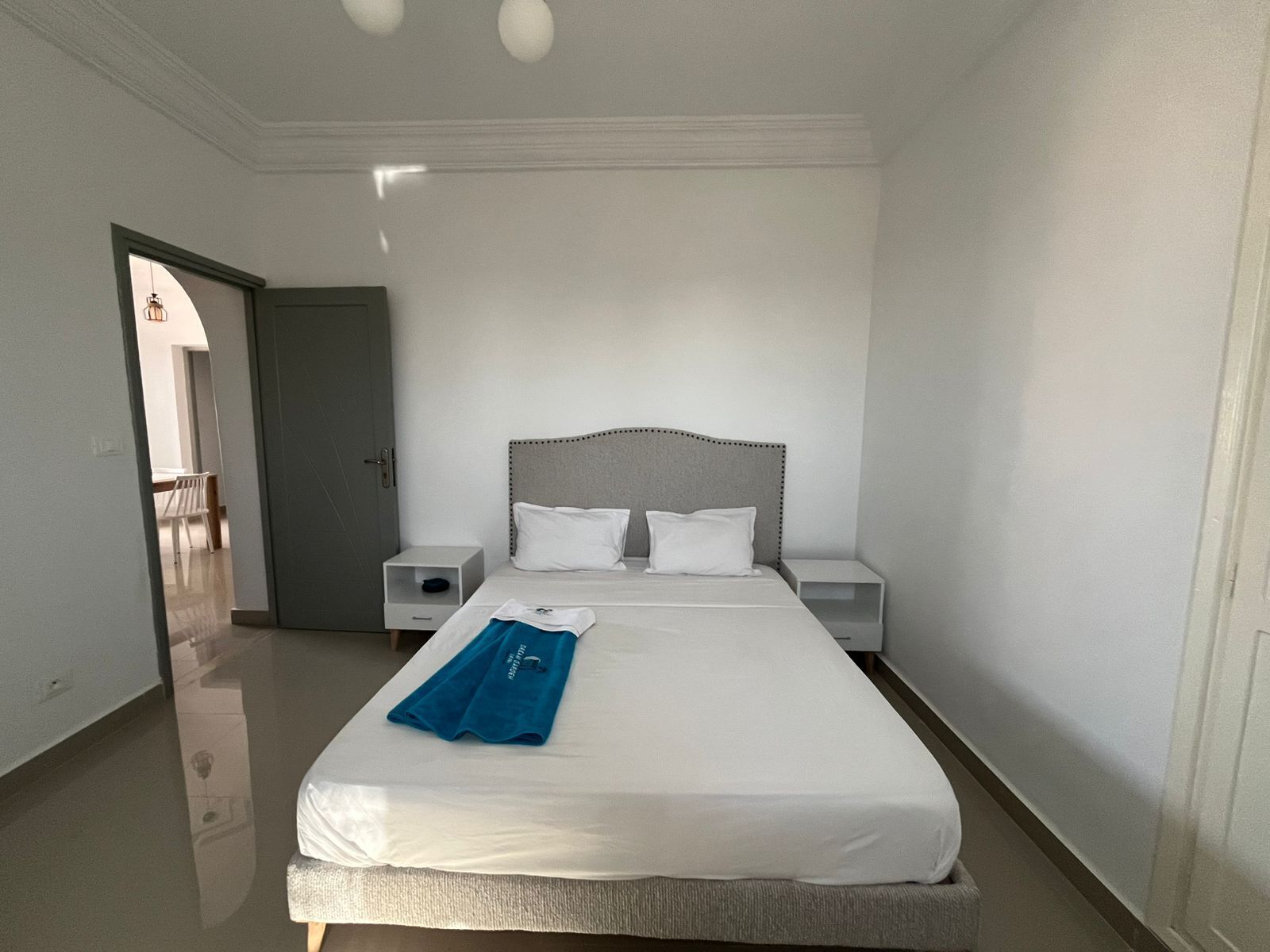 A hotel room with a large bed, two bedside tables, and a door leading to another room.
