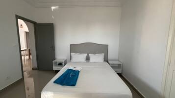 A hotel room with a large bed, two bedside tables, and a door leading to another room.