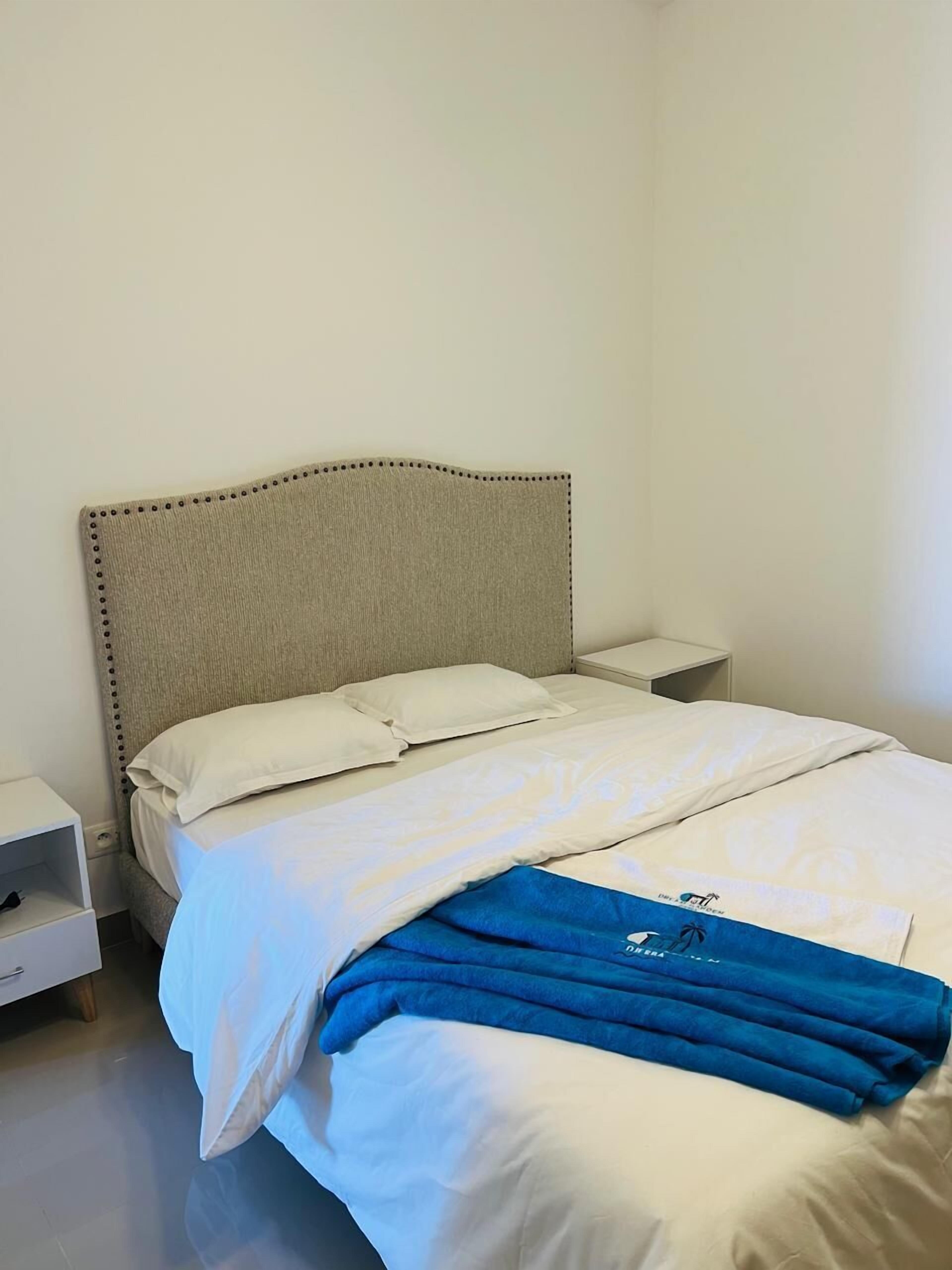 A neatly made bed with white bedding and a blue towel, a bedside table, and a nightstand.