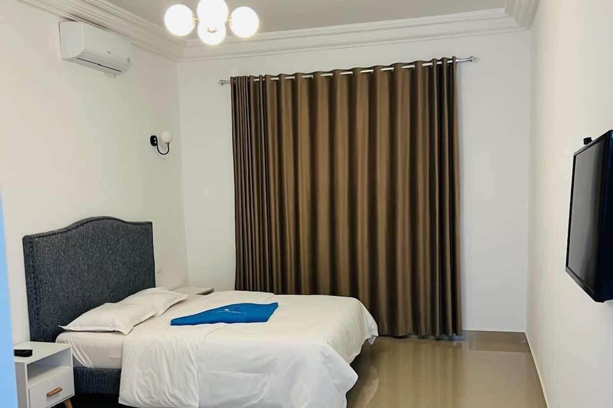 A hotel room with a bed, a nightstand, a television, and a window with curtains.