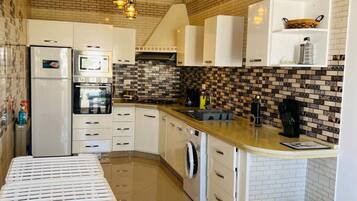 A compact kitchen with white cabinets, a built-in oven, a washing machine, and a small dining table.