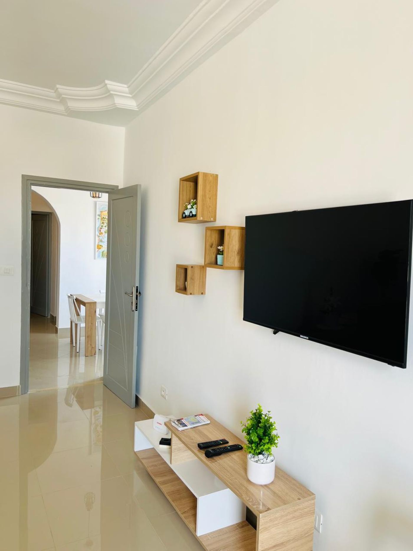A modern living room with a flat-screen TV mounted on the wall, a wooden coffee table with a plant, and a bench.