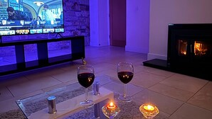 Ett vardagsrum med en tv, två glas rött vin, ett ljus och en öppen spis.