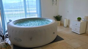 Ett spa-rum med ett stort bubbelbad, ett litet sidobord med en växt och utsikt genom ett stort fönster.