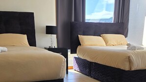 Ett hotellrum med två sängar, ett nattduksbord och ett fönster med gardiner.