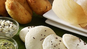 A variety of snacks including fried items and a white, round, flat bread with black seeds, served on a banana leaf. - Maryland Residency (Sulthan Bathery)