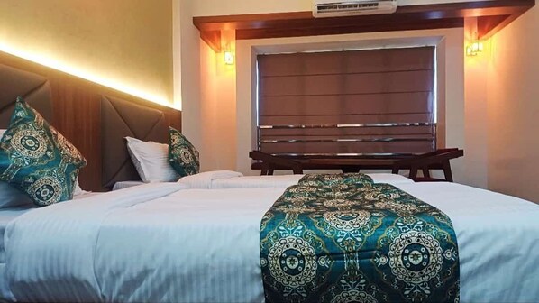 A hotel room with a large bed, a headboard with built-in lighting, and a bench against the wall.