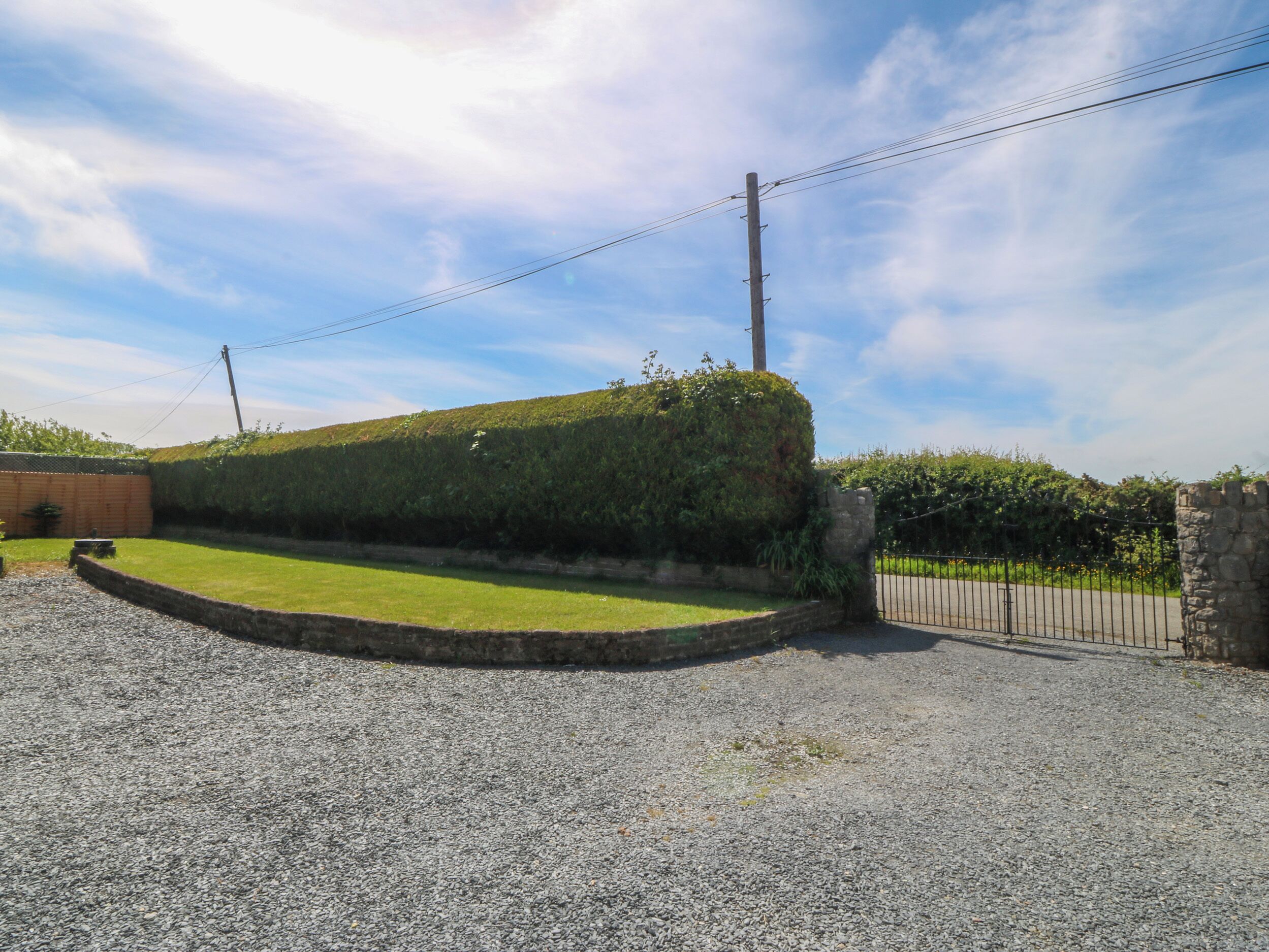 A well-maintained garden with a neatly trimmed hedge, a gravel driveway, and a stone wall.