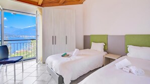 A hotel room with two beds, a chair, and a view of a lake and mountains. - Casa Zaira 1 2BR in Caviano Gambarogno (Gambarogno)