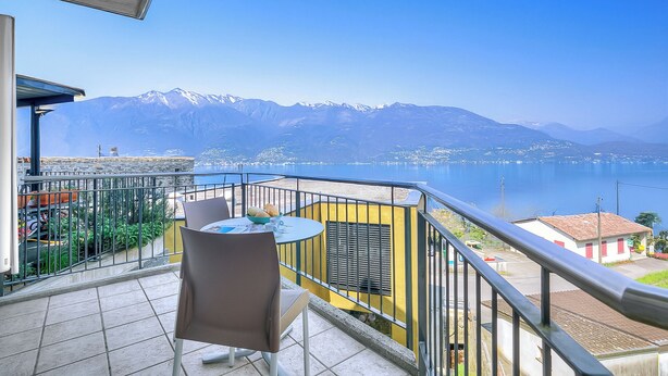 Ein Balkon mit Tisch und Stühlen mit Blick auf einen See und Berge.